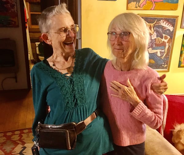 Brooke puts an arm around Janet as Janet tries to smile without revealing her teeth